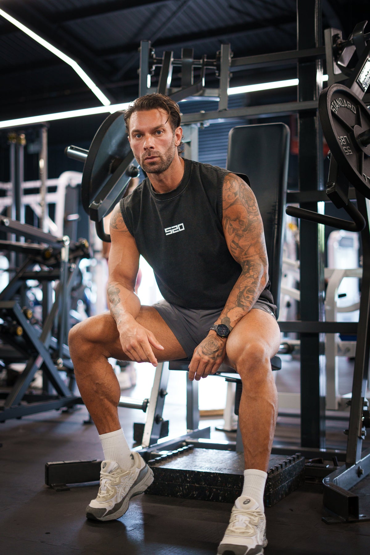 Man wearing the washed-black S20 End of Summer Vest, front view, seated — drop-armhole cut with small white S20 chest mark
