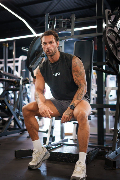 Man wearing the washed-black S20 End of Summer Vest, front view, seated — drop-armhole cut with small white S20 chest mark